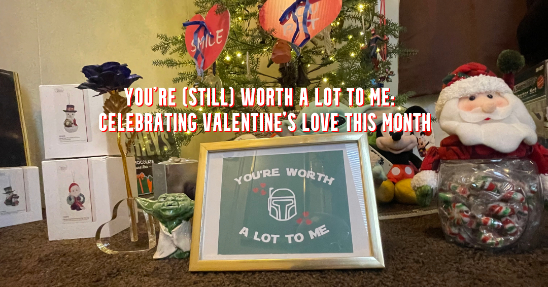 Valentine-themed display with a small decorated tree, heart ornaments, framed “You’re worth a lot to me” sign, Yoda figurine, Santa plush, Mickey Mouse, and a jar of candy.